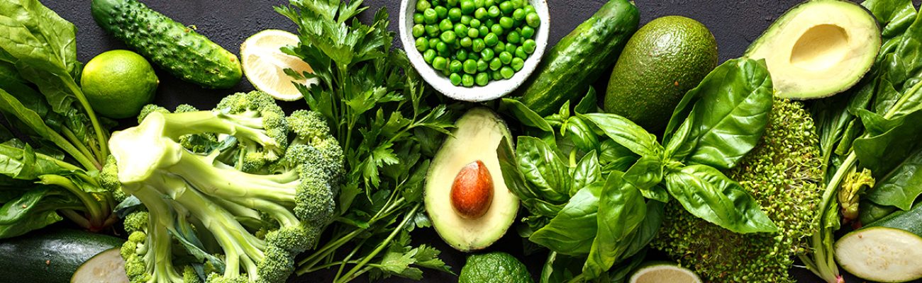 Raw healthy food clean eating vegetables: cucumber, alfalfa, zucchini, spinach, basil, green peas, dill, parsley, avocado, broccoli, lime on dark stone background, top view